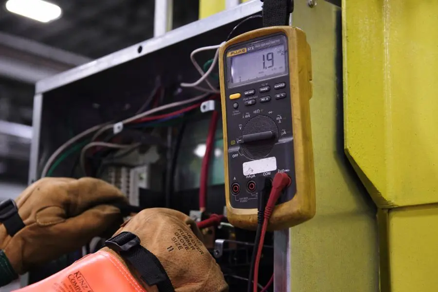 Électricien testant une installation avec un multimètre, gants de protection aux mains