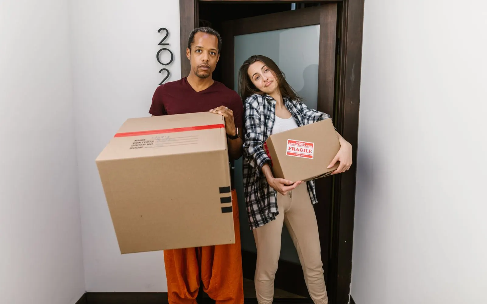 Couple portant des cartons de déménagement à l'entrée de son nouveau logement