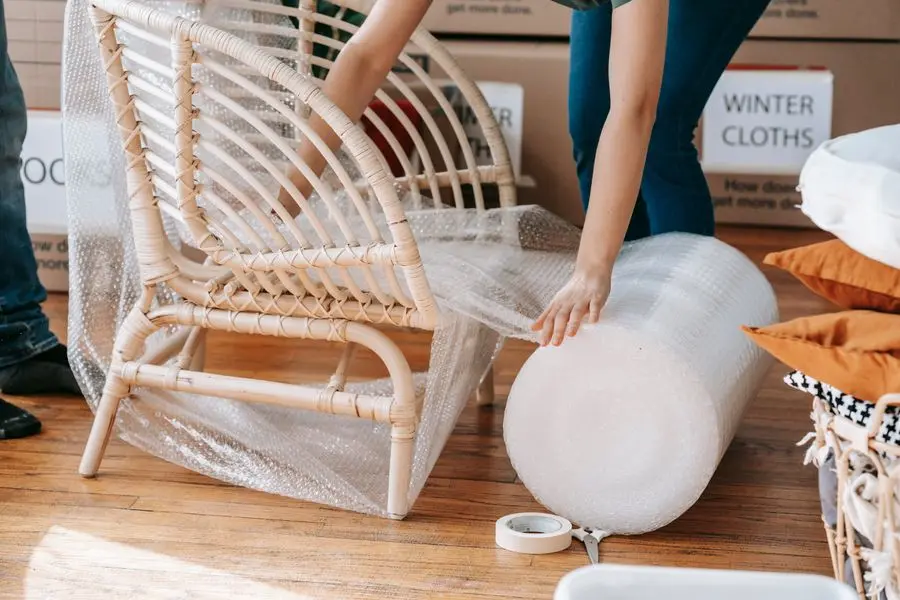 Chaise en rotin protégée avec du papier bulle avant un déménagement, entourée de cartons étiquetés