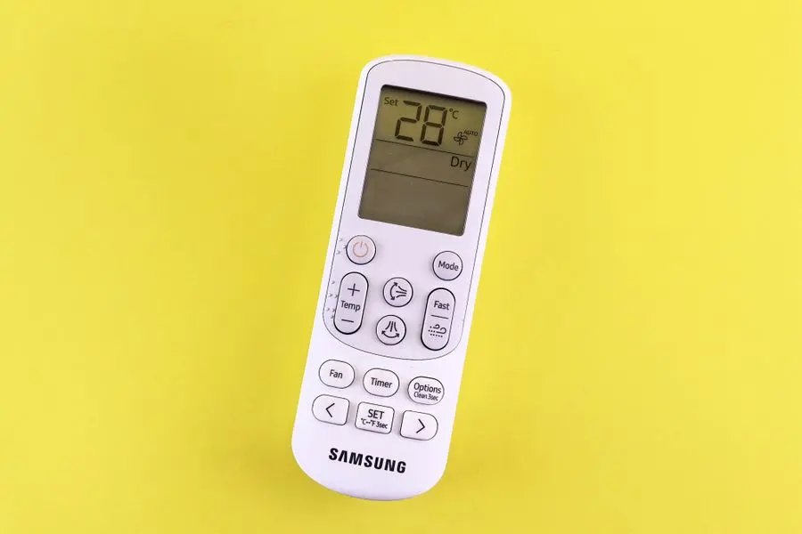 Télécommande de climatiseur réglée sur 28°C tenue devant un fond jaune