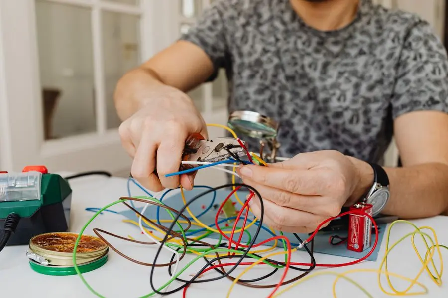 Mains dénudant et raccordant des fils électriques multicolores à l'aide d'une pince sur un plan de travail