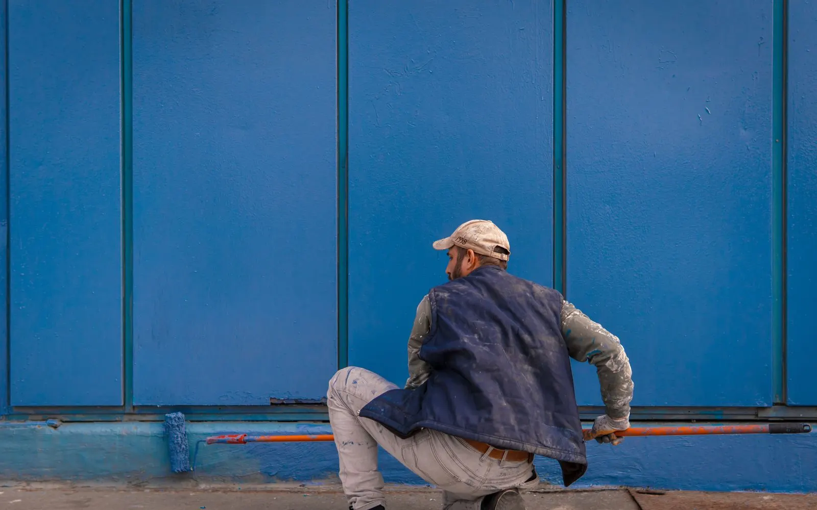 Peintre appliquant une peinture bleue au rouleau sur un mur extérieur